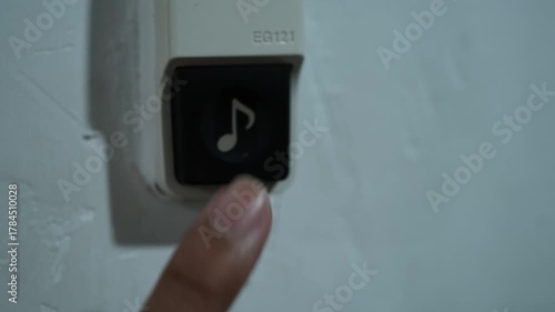 Close-up of a person's finger pressing a black elevator call button on a white wall-mounted panel
