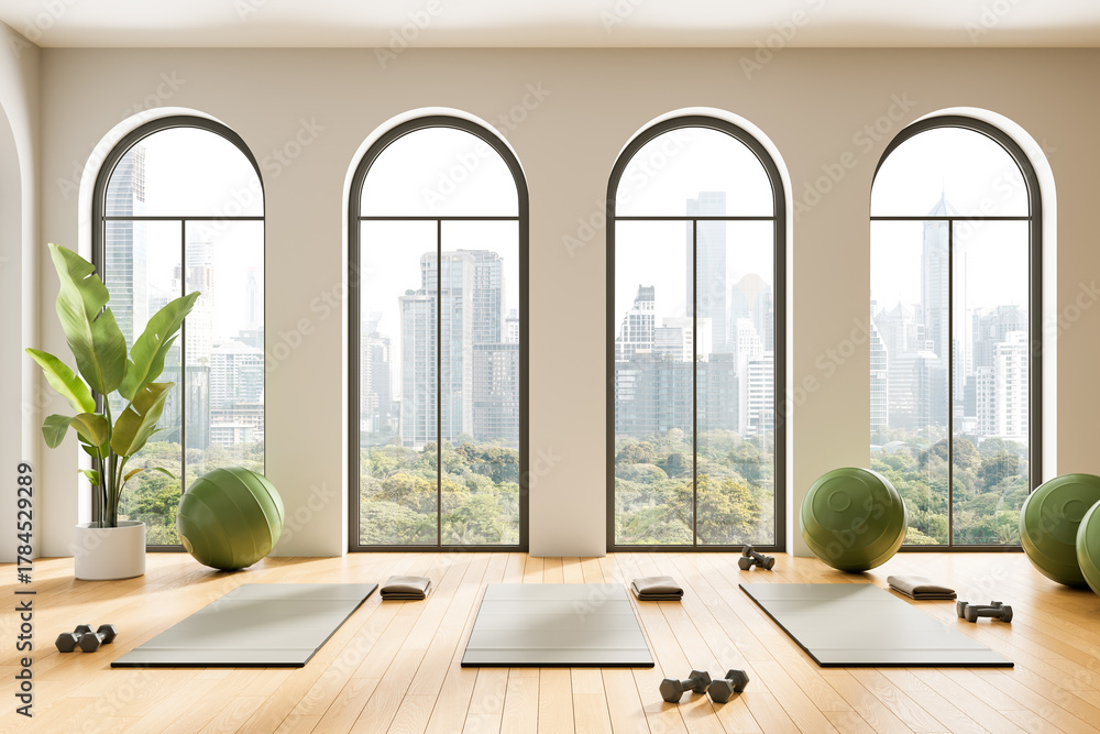Obraz premium Modern yoga studio interior with arched windows, wooden floor and city view, fitness mats and green exercise balls arranged in minimalist design. 3D Rendering