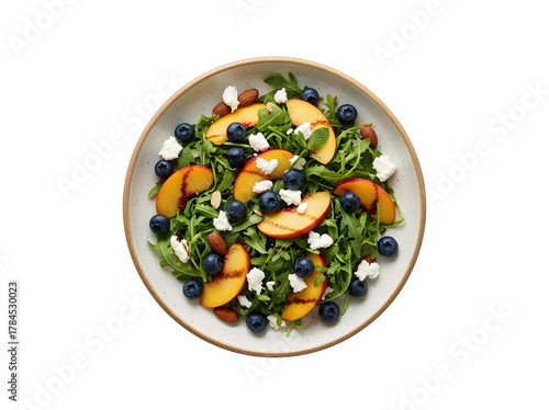 A fresh fruit salad featuring peach, blueberry, and arugula, topped with cheese and almond nuts, seen from above

