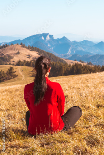 A young girl sits on the ground and looks at the beautiful panorama of autumn mountains