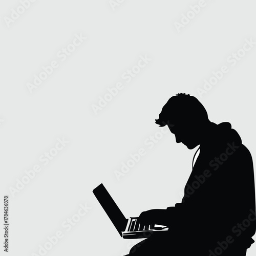 A dark silhouette of a person intently working on a laptop against a plain light background.