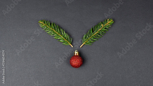 Reindeer concept made with fir branches and red Christmas ball decoration on black paper background