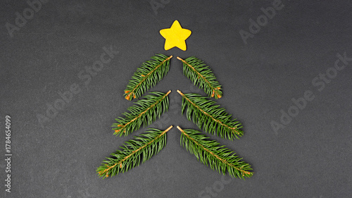 Christmas tree concept made with fir branches and yellow star decoration on black paper background