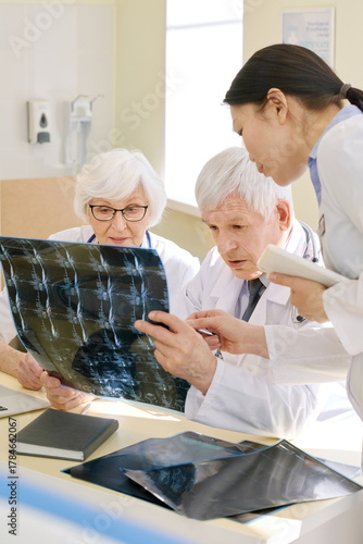 Group of experienced doctors looking at X-ray of patient after MRI examination and analyzing results together in consulting room