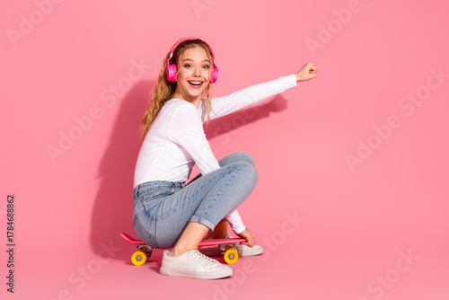 Εκτύπωση καμβά Young girl sitting on a pink skateboard wearing headphones, smiling brightly aga