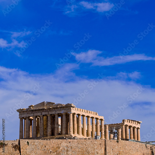 Parthenon, a monumental symbol of Western civilization  atop the fortified Acropolis hill against a blue sky scattered with clouds, emphasizing the scale and significance of the ancient structure.