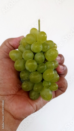 A close-up shot of a hand gently holding a vibrant bunch of fresh green grapes against a bright white background