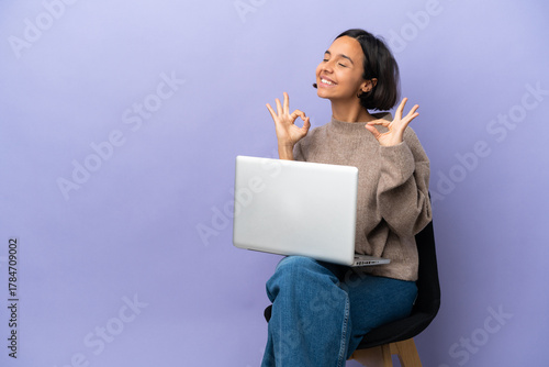 Young mixed race woman sitting on a chair with laptop isolated on purple background in zen pose
