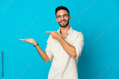 Fotografie Young caucasian man isolated on blue background holding copyspace imaginary on t