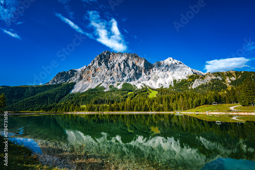 Panoramablick auf die Zugspitze mit dem See im Vordergrund und leichte Wolken bei einem sonnigen Sommertag