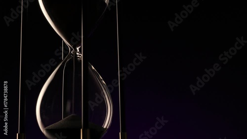 dark hourglass with fine sand flowing, a metaphor for the irreversible passage of time and life�s fragile continuity.