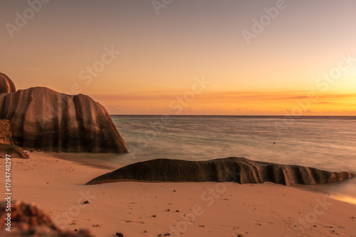 Romantic sunset at Anse Source d’Argent, with golden light reflecting on the turquoise water, iconic granite boulders, and a dreamy tropical beach setting
