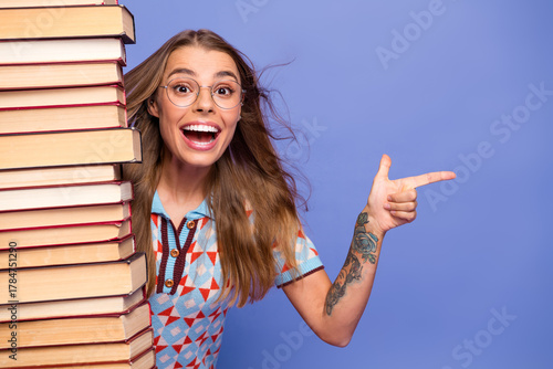 Young woman with stack of book smiling and pointing against purple background