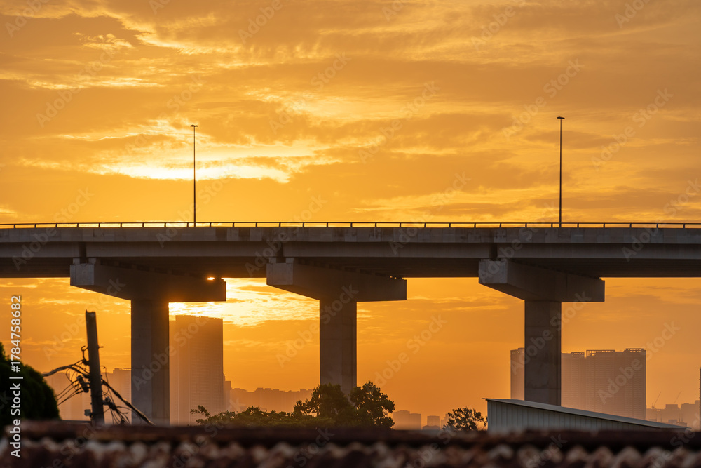 Obraz premium Golden sunset over urban bridge and highway pillars at dusk with silhouetted city