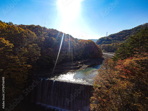 Autumn colors in a valley with a weir, bright sun and lens flare