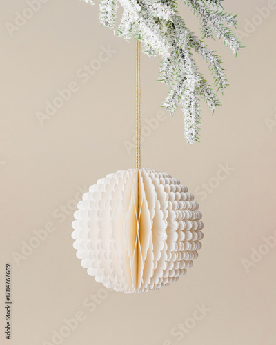 Paper Christmas ornament, white New year ball hanging on string on snow green fir tree branch on beige background. Christmas bauble, minimal aesthetic winter holiday xmas eco friendly decoration.