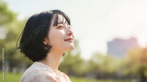 晴れた日の公園で柔らかな笑顔で空を見上げる美しい女性