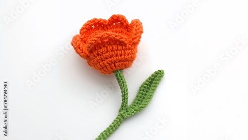 Crocheted Floral Creation, Orange Blossom with a Green Stem on a White Surface.