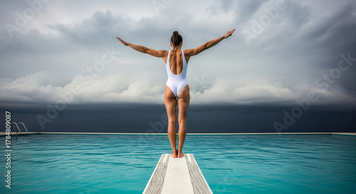 Woman in White Swimsuit Ready to Dive Off Diving Board into Swimming Pool Against Stormy Sky.