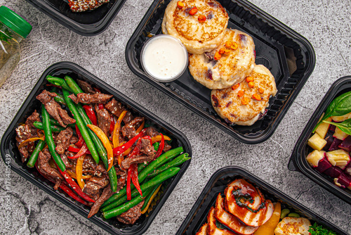 Nutritious meal prep containers with beef stir fry, pancakes, grilled chicken, and salad on gray background