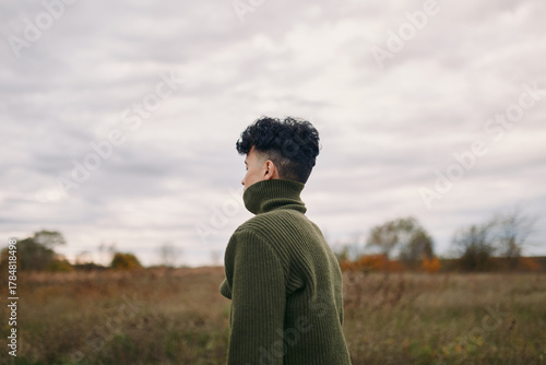 A candid image emphasizes authenticity as a single figure in a green knit turtleneck stands in a wide field, back turned, inviting honest interpretation and quiet focus.
