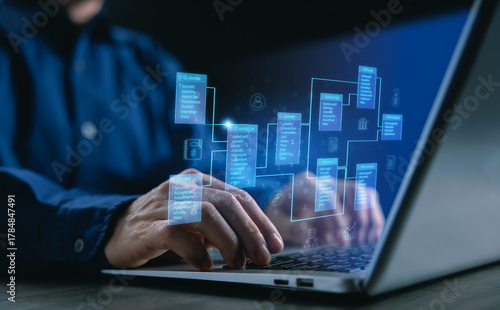 A software developer working on a laptop with a holographic database schema, representing data management, information system, cloud computing, and digital innovation for modern business solutions.