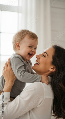 Happy mother holding her laughing toddler son at home. Vertical portrait of a joyful family sharing a loving moment. Motherhood and childhood happiness concept