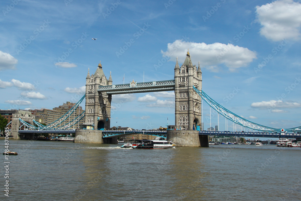 Obraz premium Tower Bridge stands tall over the River Thames on a sunny day in London with boats floating nearby