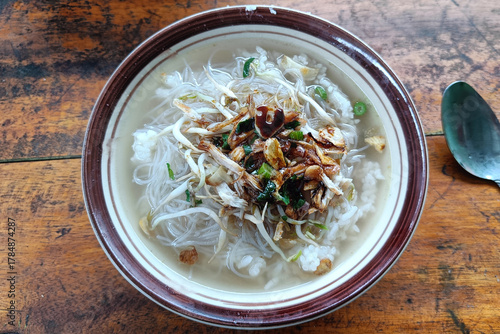 A steaming bowl of chicken porridge (Bubur Ayam or similar), served with sliced meat and crispy crackers.