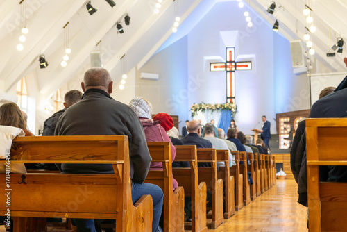Fotografía Congregation of diverse individuals seated in wooden pews, attentively listening