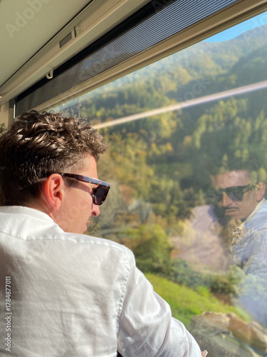 a man sitting on a train looks at the landscape from the window.