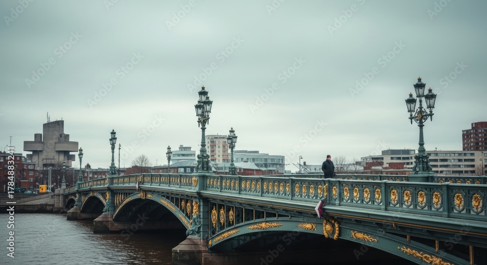 Fototapeta premium Ornate historic bridge over a city river. Solitary adult male walking across the urban crossing. Cinematic cityscape with a moody atmosphere. Concept of journey and urban exploration