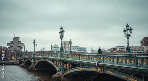 Fototapeta Naklejka Na Ścianę i Meble -  Ornate historic bridge over a city river. Solitary adult male walking across the urban crossing. Cinematic cityscape with a moody atmosphere. Concept of journey and urban exploration