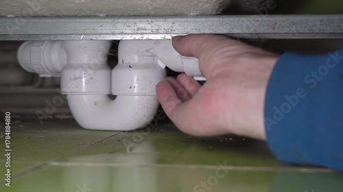plumber disconnects the siphon under the bathtub, repair the siphon under the bathtub, plumber's hands unscrew the siphon under the bathtub, clogged siphon in the bathtub