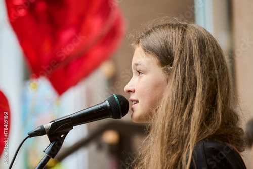 Young girl speaking into microphone with red heart balloons in background