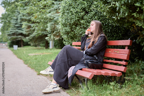Young woman enjoying coffee on red bench in green park setting