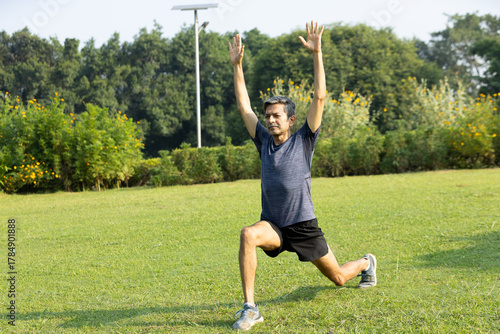 Energetic Indian Senior Man Performing High Lunge Stretch with Arms Raised in Park