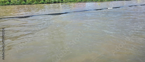 The curb is flooded. The river water has overflowed the road so that the edge of the road cannot be seen. Water has waves caused by the force of passing cars. Cars cannot drive through. Dangerous 
