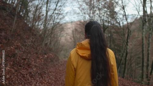 Slow motion camera follows active young brunette woman hiker in yellow jacket walking alone in the forest. Girl walking and enjoying outdoors nature in late autumn season