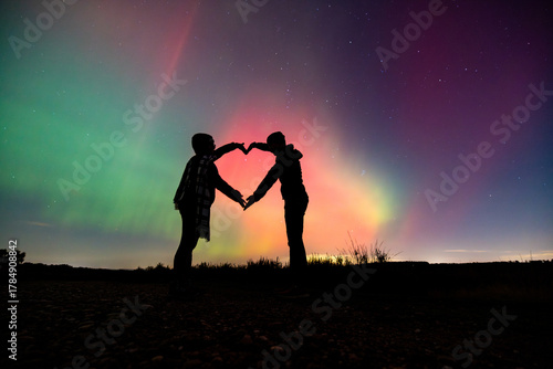 Couple hands forming heart during aurora borealis display