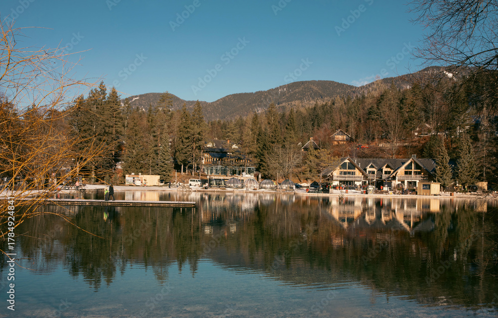 Obraz premium Kranjska Gora, Slovenia - January 04, 2024: Scenic view of tranquil Jasna lake reflecting mountains and charming lodges in Triglav National Park, showcasing the beauty of the Julian Alps landscape