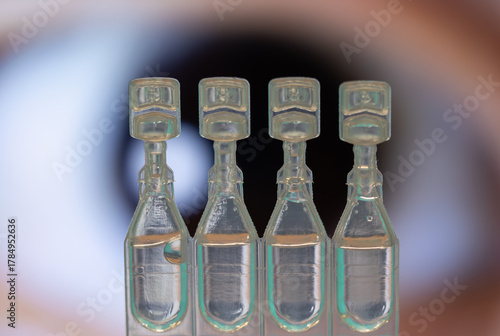 A row of single-dose artificial tear vials focused in the foreground with a blurred human eye in the background.