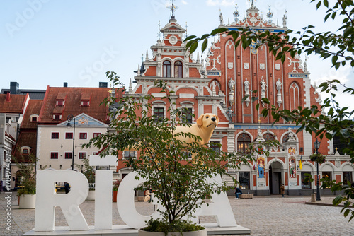 View of the Riga sign with a decorative dog sculpture in the historic center of Riga, Latvia. The scene features traditional European architecture and a well-known city landmark located near Riga Old 
