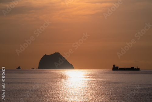 See the silhouette of a cargo ship sailing near Keelung Islets at Waishuangxi, Taiwan. Filmed on June 23, 2025, during a calm summer morning.