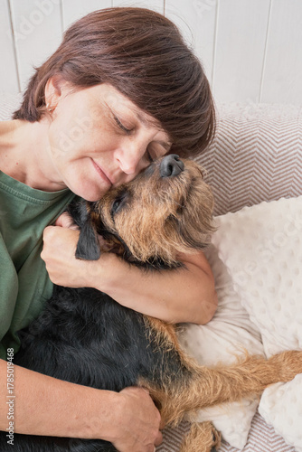 Mature caucasian woman embracing dog affectionately on sofa.