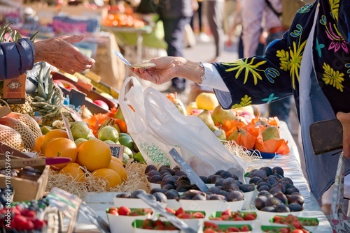 Client qui paye son achat de fruits et légumes frais sur un marché ensoleillé de Nice