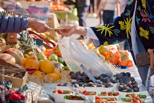 Client qui paye son achat de fruits et légumes frais sur un marché ensoleillé de Nice