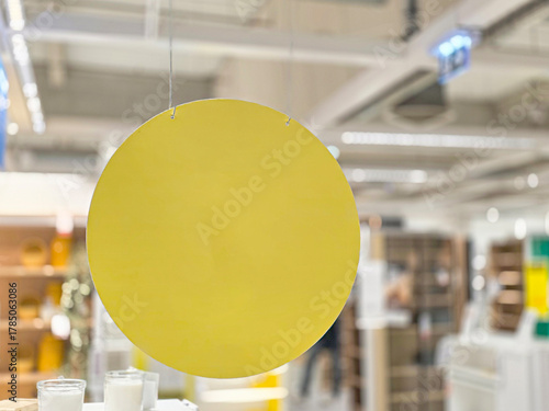 A bright yellow circular display sign hangs from the ceiling of a modern retail store, surrounded by shelves filled with various home decor items.