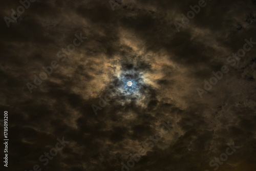 Moon shines through clouds with dramatic blue and gold colored halo 