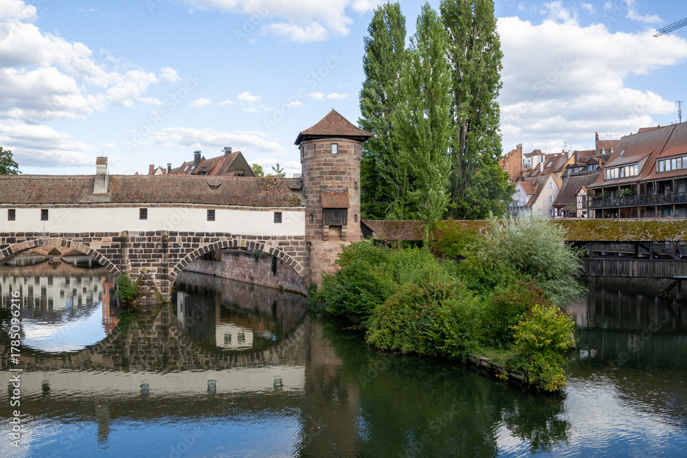 Fototapeta premium Picturesque view of Henkerhaus Museum, Wasserturm, and the Henkersteg bridges in Nuremberg, Bavaria, spanning the Pegnitz River amid charming medieval architecture.